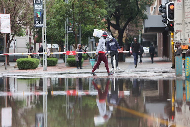 A street vendor walks next to a flooded road in Newtown after overnight and morning showers in Johannesburg.