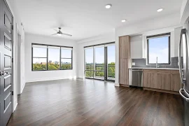 Apartment interior featuring large windows, wood-style floors, and a sleek kitchen with stainless steel appliances.