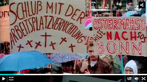 Bild aus Video: Protestierende mit Pappschildern «Schluss mit der Arbeitsplatzvernichtung! (Verziert mit Todeskreuzen)», «Ostermarsch nach Bonn. Hilfe. SOS».