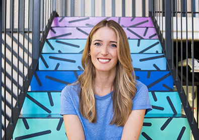 Founder Andrea Barber smiles in front of a colorful staricase