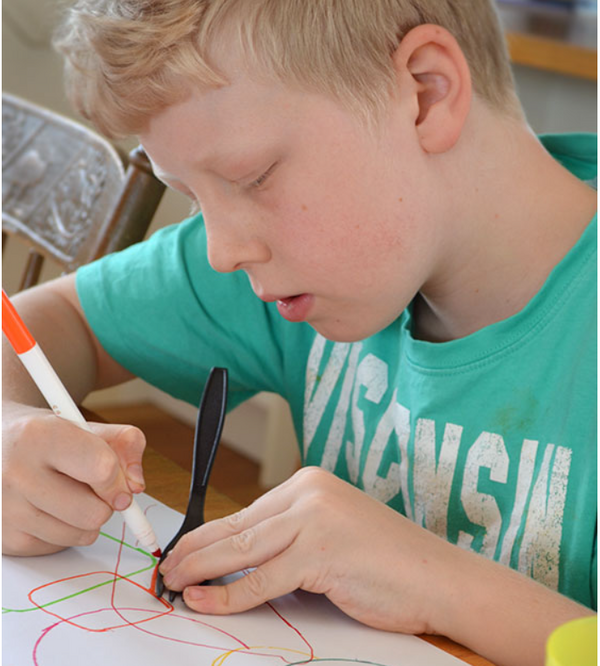 A child tracing a fork and drawing it on a paper