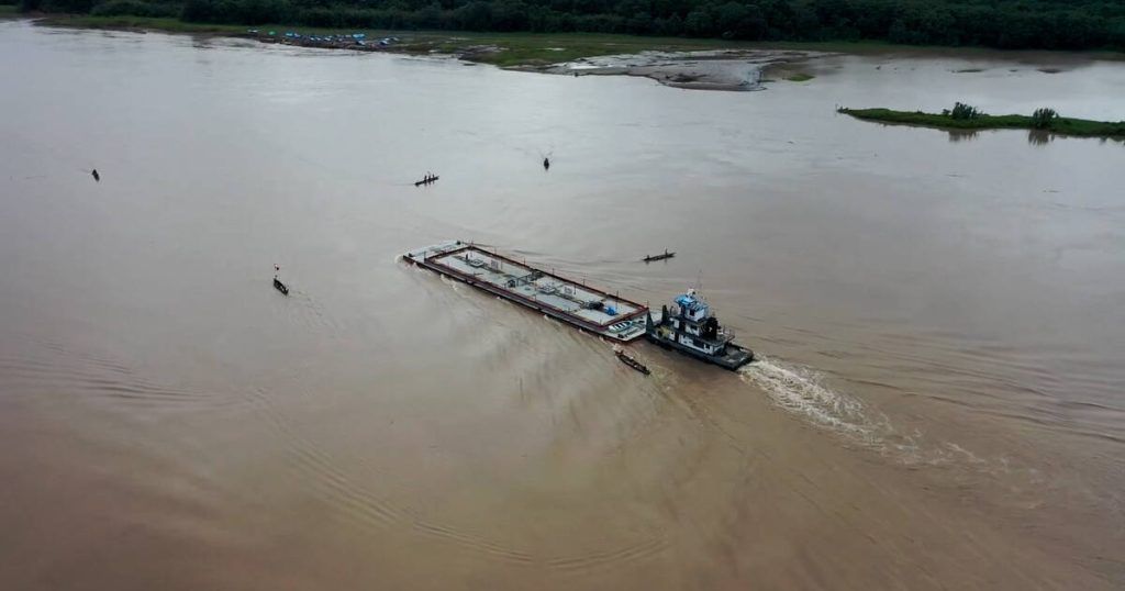 A large oil tanker is surrounded by small canoes on a wide stretch of river