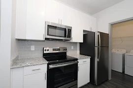 Kitchen with tile backsplash, microwave, glass top range/oven, refrigerator, and laundry closet with full washer and dryer