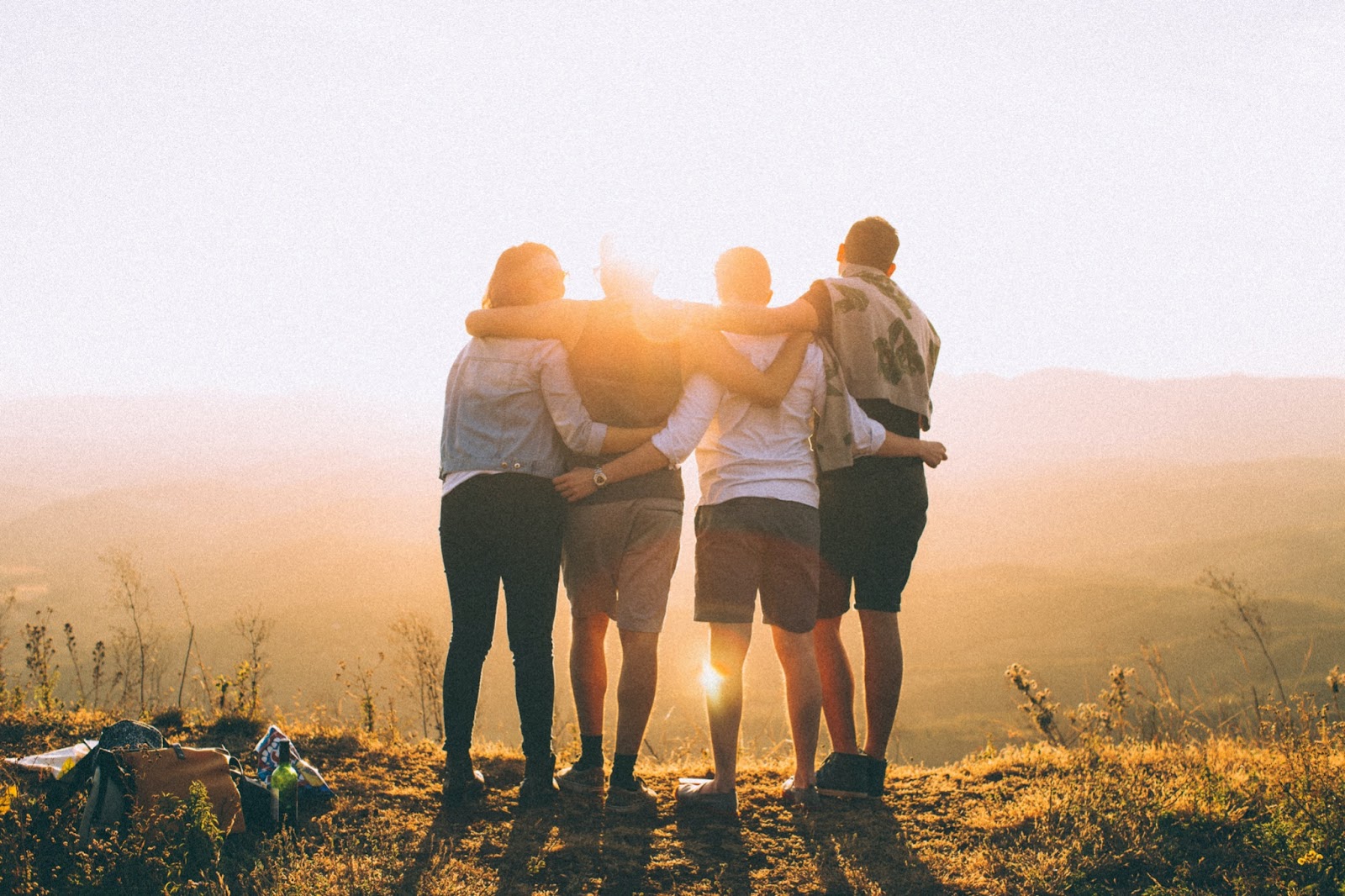 Four friends hugging in a field watching a sunset.