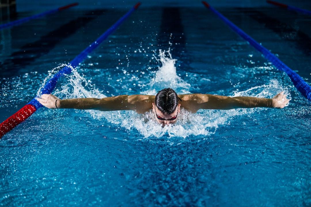 A man wearing swimming goggles doing the breast stroke in a swimming pool with wat