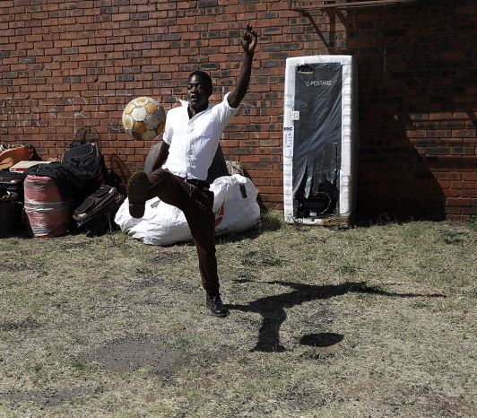 A displaced foreigner passes time with a solitary game of soccer outside a community hall in Katlehong.