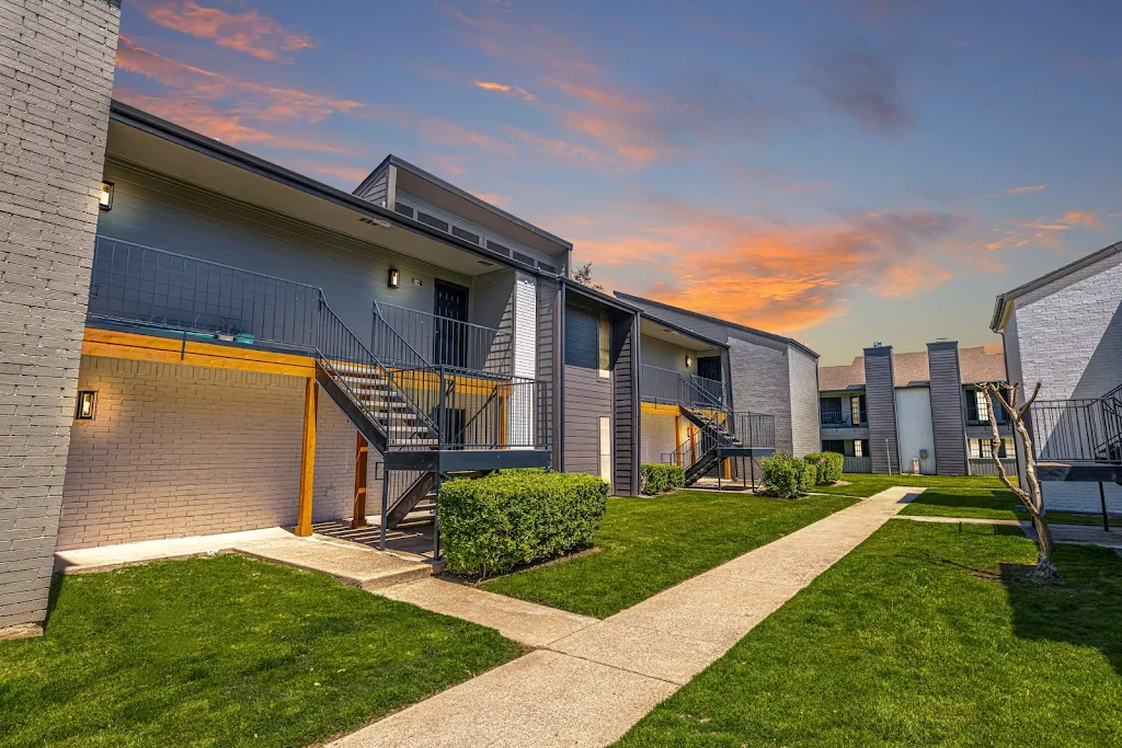 Modern apartment complex at twilight with vibrant sunset sky in the background, featuring exterior stairs and green lawns.