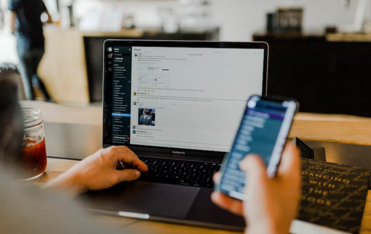 image of a person using their phone and laptop in a cafe