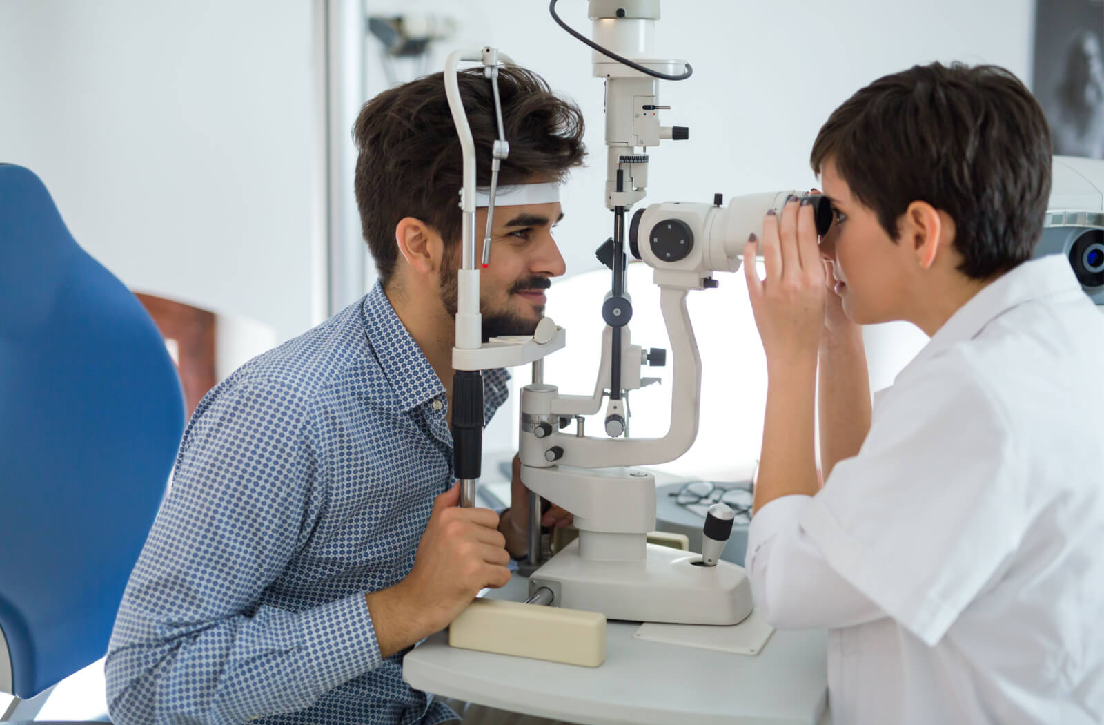 A female optometrist examining the eyes of a young man using a medical device to detect potential eye problems