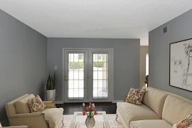 Modern apartment living room with neutral-toned furniture, glass door with blinds, and wall art.