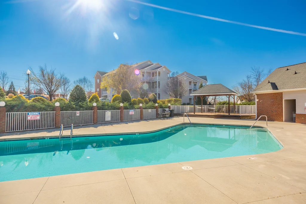 Community swimming pool surrounded by concrete deck and iron fence with apartment buildings in background