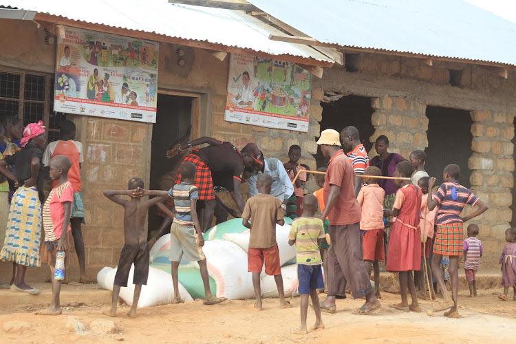 Hungry pupils and parents with bags of maize and beans donated by Childcare Society to Loyeya Primary School in Tiaty, Baringo county, on Monday