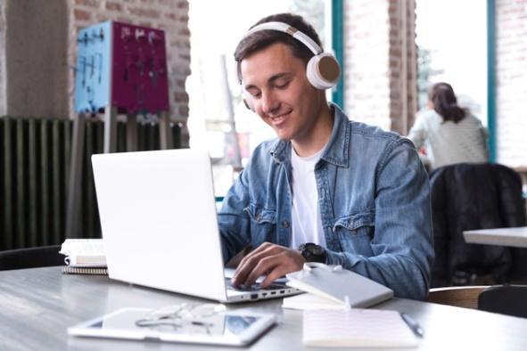 Teenage student in headphones sitting at table and typing on notebook Free Photo