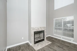 Living room with tiled fireplace, two windows with blinds, tall ceilings, wood plank floors, gray walls, and white trim