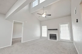 Living room with carpet, a fireplace between a large window and a patio door, and a ceiling fan near skylights.