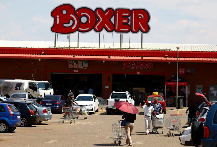 Shoppers walk outside Boxer, one of South Africa's fastest-growing discount grocery chains, in Protea Glen, west of Johannesburg, on November 25 2024.