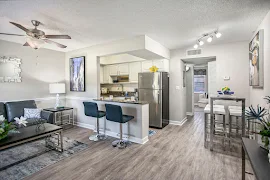 Modern apartment interior with living space, kitchen, and dining area, featuring sleek furnishings and bright lighting.