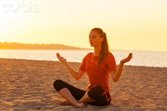 People practising yoga on beach, lotus pose, hands raised