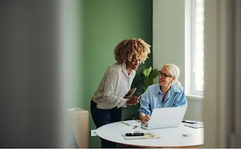 Dos mujeres mirando un portátil mientras hablan de trabajo.