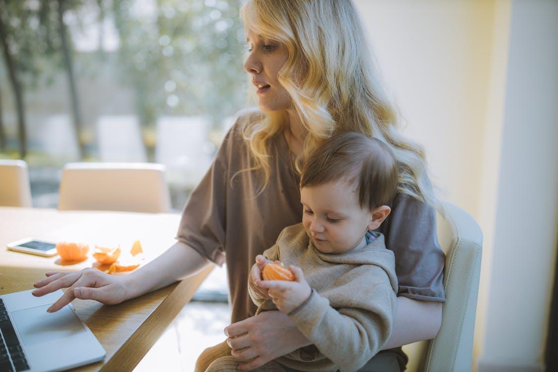 Woman Carrying her Baby and Working on a Laptop