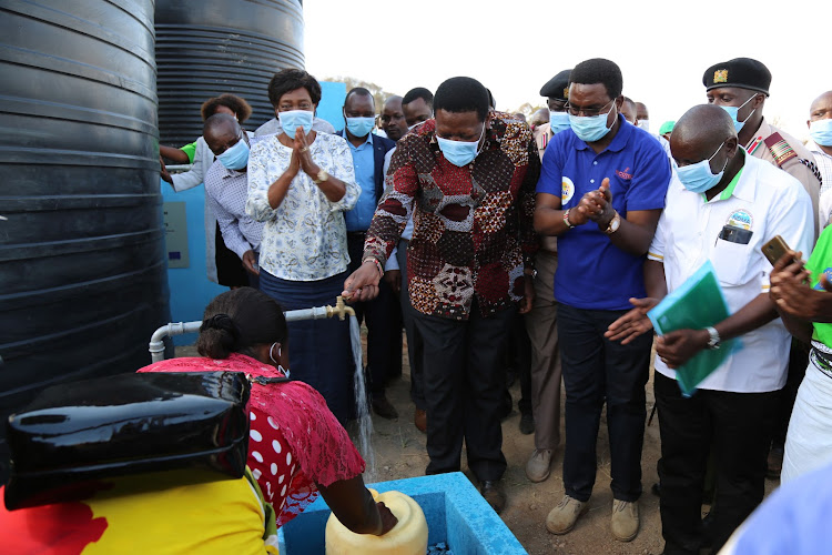 Devolution CS Eugene Wamalwa turns on a tap to commission the Kwa Ndaki earth dam in Kitui South on Wednesday. Looking on are Governor Charity Ngilu and other guests.