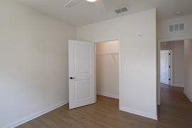 Bedroom with wood plank flooring, tan walls, white trim, and a white door to a closet 