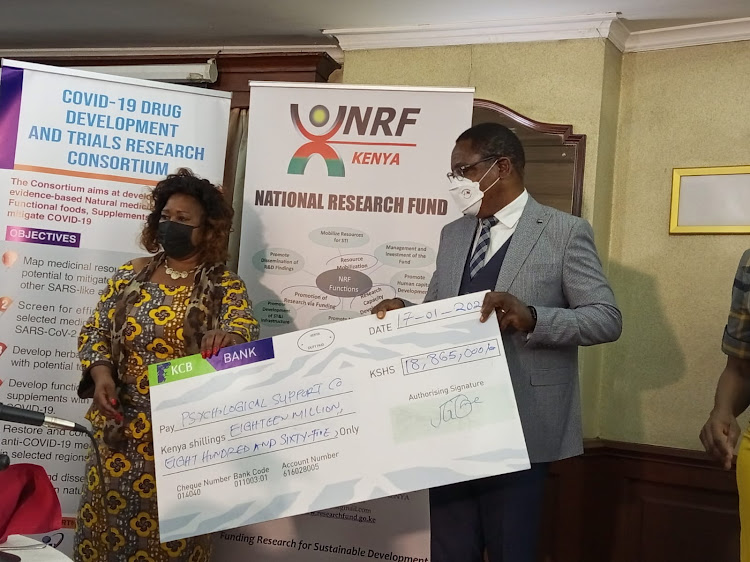 Chair National Assembly departmental committee on education and research Florence Mutua and University Education PS Simon Nabukwesi hold a dummy cheque during the handover in Nairobi on January 17.