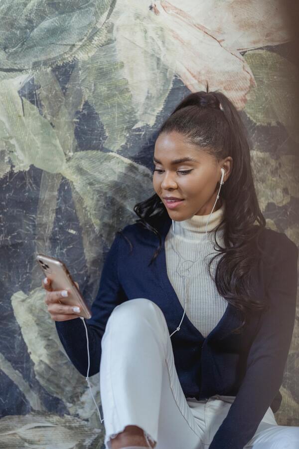 Mulher negra sentada, com fone de ouvidos e usando o celular
