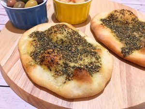 A couple delicious Lebanese flatbread on a cutting board along with olives and hummus.