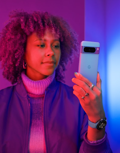 A person holds their Pixel phone in Bay colour. They stand in a room with purple and red lighting.