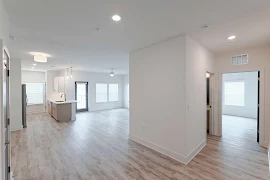 Apartment entry door open to the kitchen, dining, and living areas with a hallway to the bedrooms 