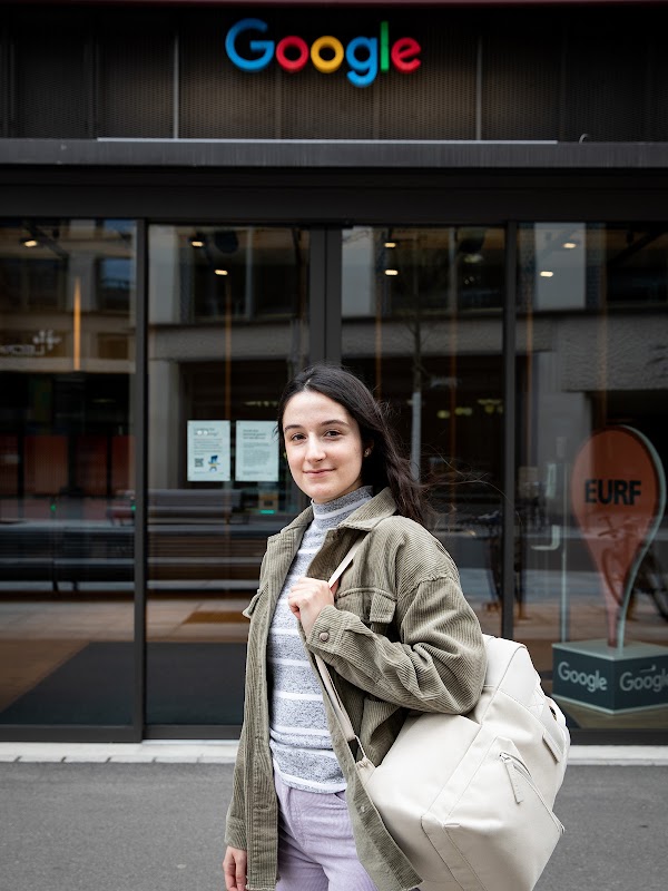 Daniela Simões, une ancienne apprentie chez Google, est devant un bureau de Google. Elle a des cheveux longs et noirs et porte un sac à dos gris.