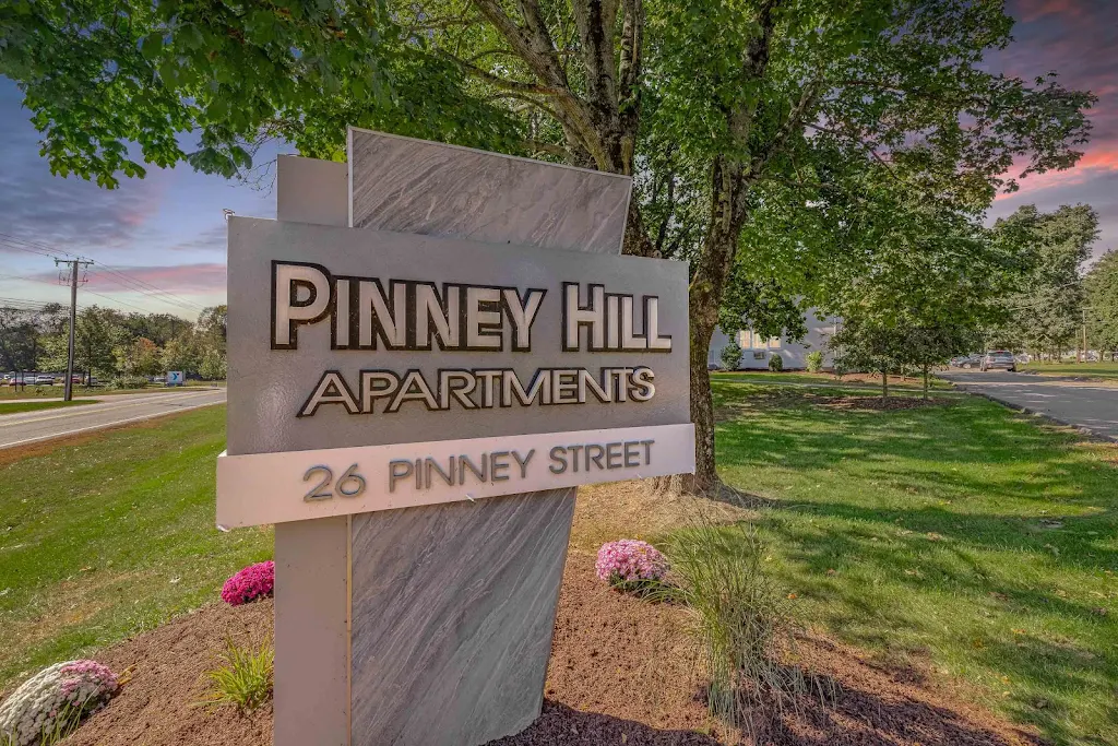 Property sign with landscaping and a shade tree in the background at dusk.