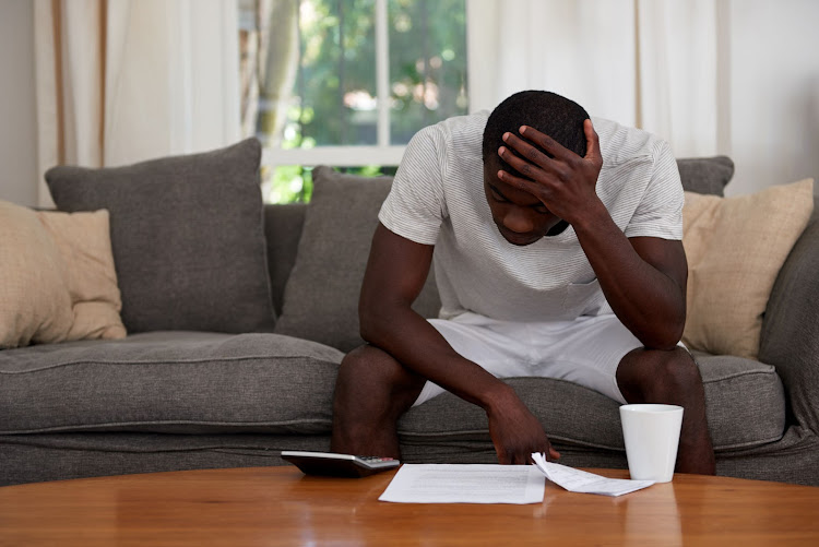 Troubled man sitting on the couch calculating home bill finance debt in his living room.