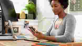 A woman seated at her desk, looking at the screen of an Android-enabled phone.