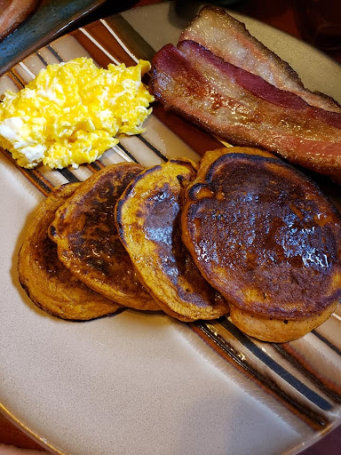 Pumpkin Pancakes covered in pure maple syrup with thick sliced bacon and cheesy eggs