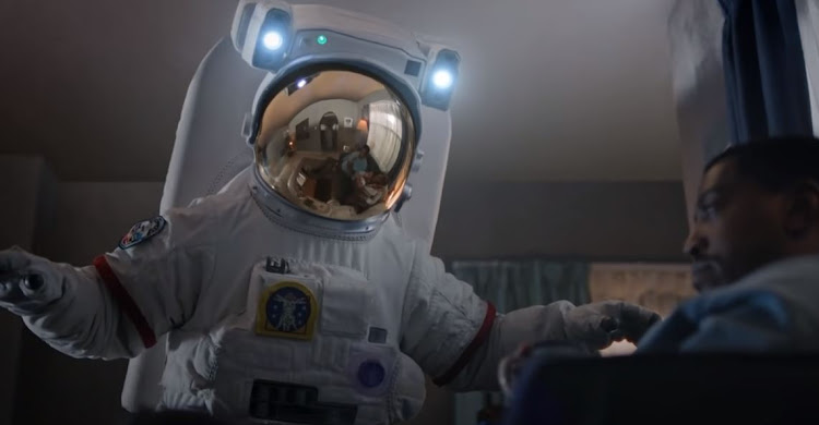 A still from the Standard Bank ad shows a father blocking the passage of his daughter - dressed as an astronaut - through his lounge.