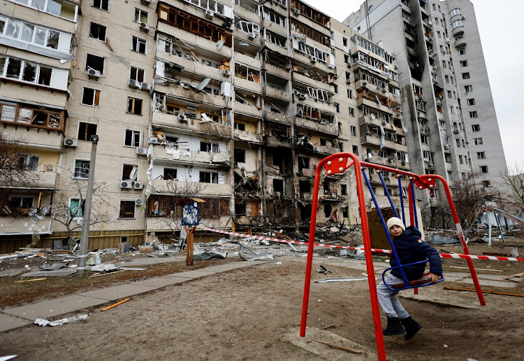 A child sits on a swing in front of a damaged block of flats in Kyiv after Russia launched a massive military operation against Ukraine.