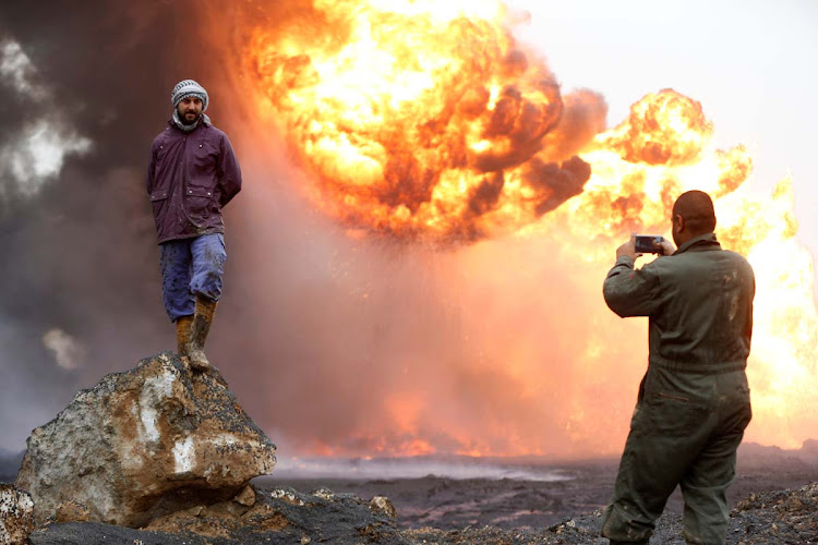 A man takes a photograph of his friend as thick smoke rises from a fire, which broke out at oil wells set ablaze by Islamic State militants before they fled the oil-producing region of Qayyara, Iraq, January 28, 2017.