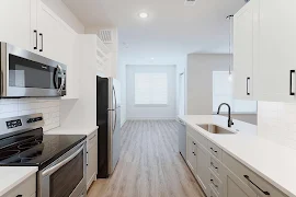 Kitchen, looking into dining room, with white quartz countertops, tile backsplash, gray cabinets, and stainless appliances