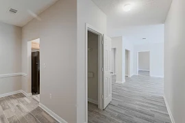 View of entry hallway with coat closet, view to kitchen, wood plank floors, grey walls, white trim