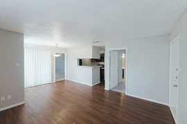 Living room, looking into kitchen, with sliding glass patio door with blinds, dark wood plank flooring, and light gray walls