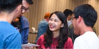 Woman in focus conversing with 2 men in soft focus, similing.