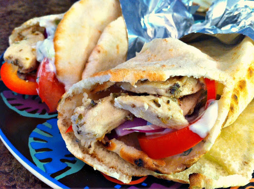 Two gyros filled with chicken and red peppers on a plate.