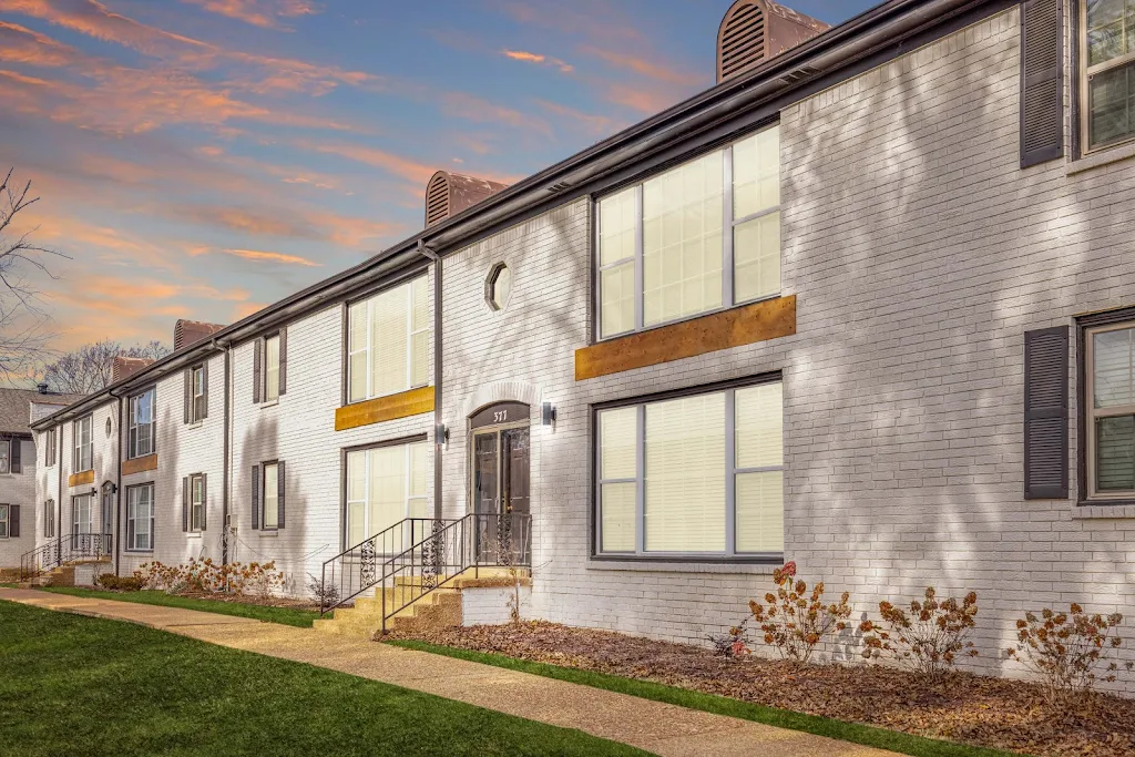 Apartment building exterior with light painted brick and landscaping at dusk.