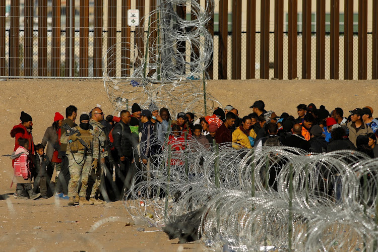 Migrants seeking asylum in the United States gather near the border wall after crossing a razor wire fence deployed to inhibit their crossing into the United States, while members of the Texas National Guard stand guard, as seen from Ciudad Juarez, Mexico January 2, 2024. REUTERS/Jose Luis Gonzalez