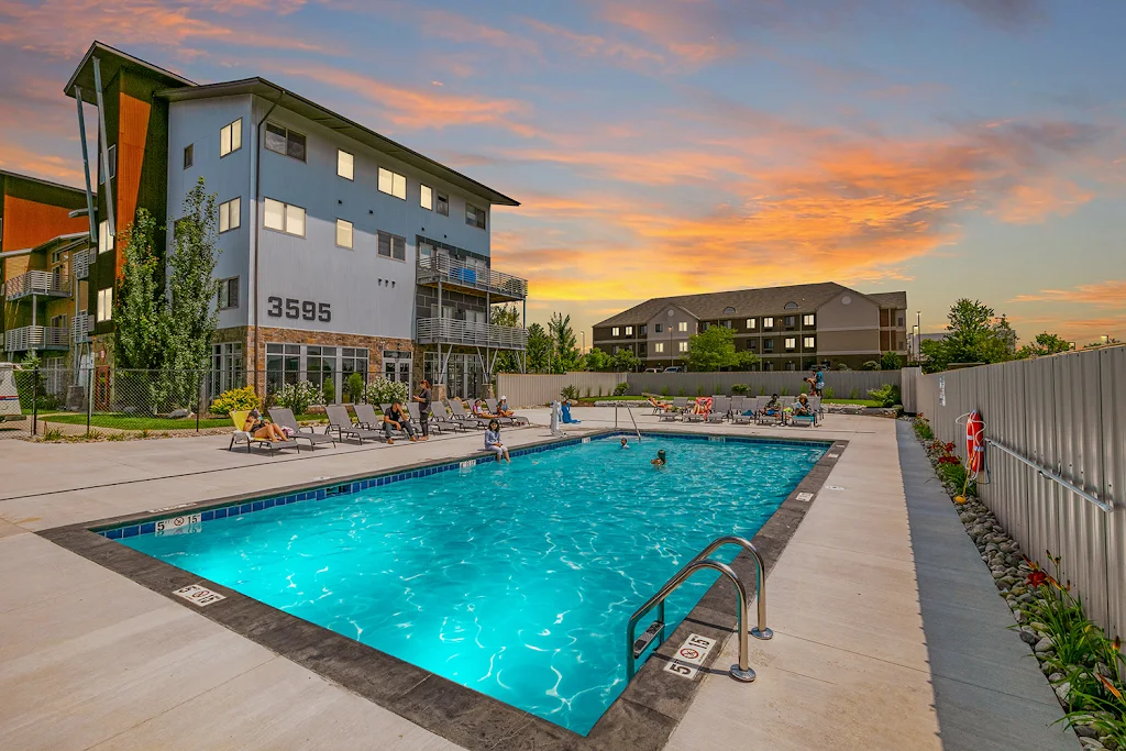 Elevation's rectangular swimming pool at dusk, next to apartment buildings, with several people and lounge chairs