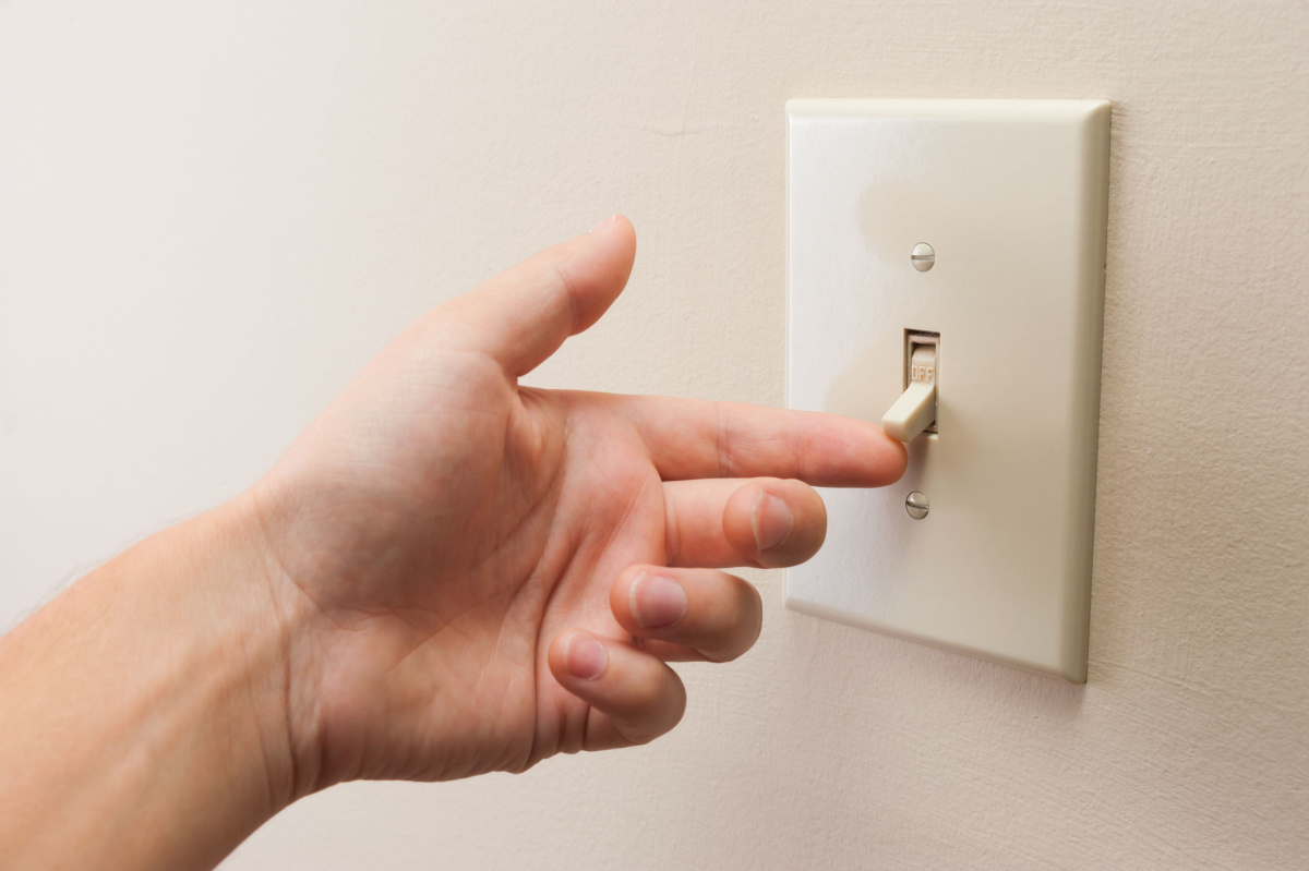 A hand flicking on a standard lighting switch.