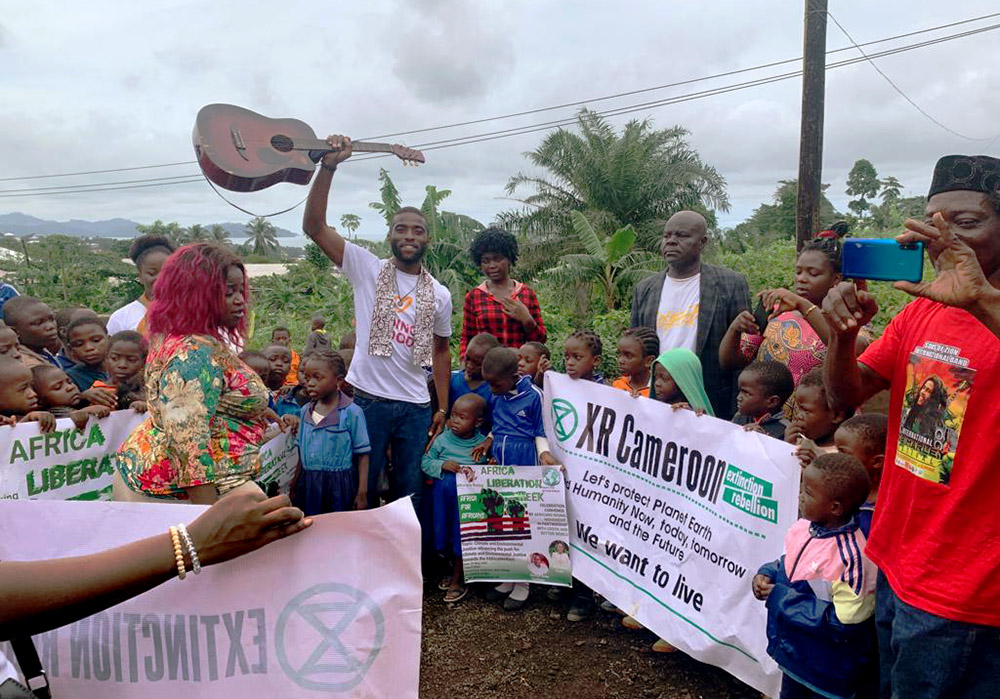 A rebel holds up his guitar while surrounded by school children holding XR Cameroon signs