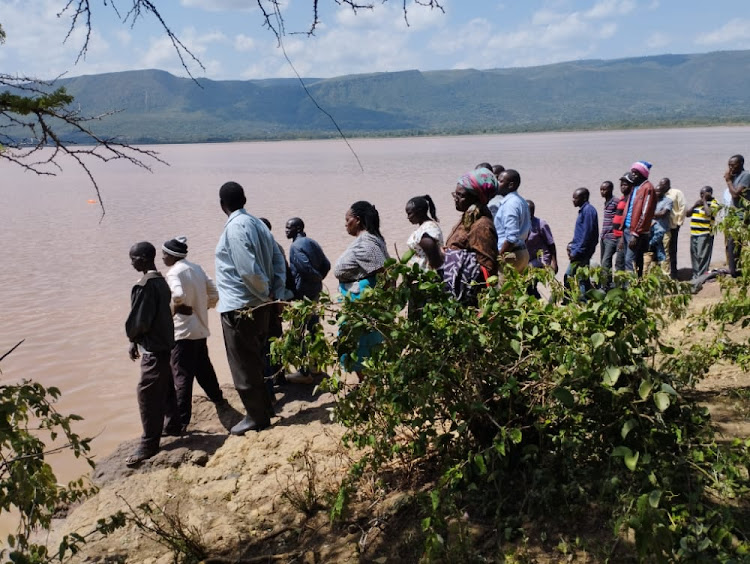 People milling around the lake waiting for the body of the pupil to be retrieved.